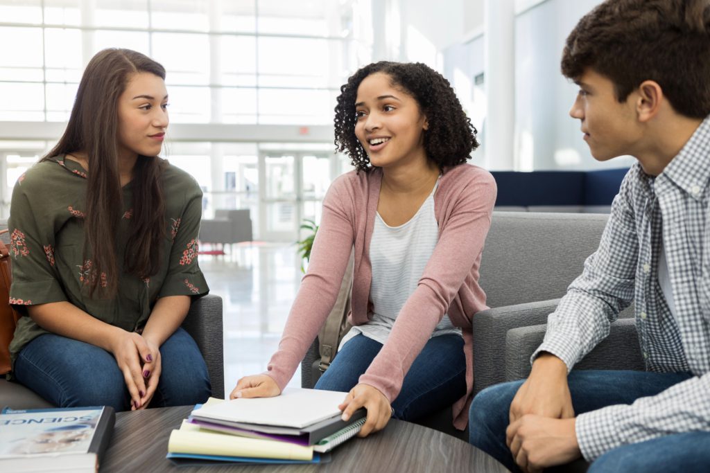 Three teenagers sit at a coffee table planning their homework together