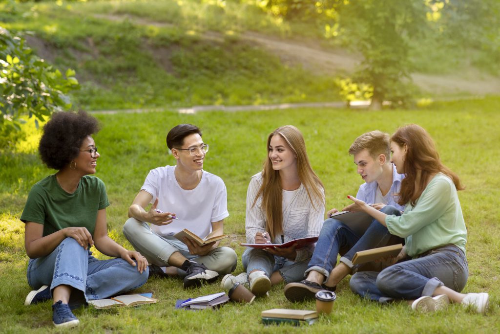 Five teenagers sit in a park doing their homework together