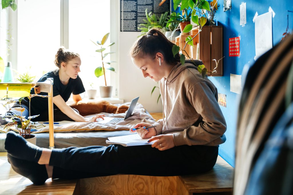Teen girl sits on a desk while wearing air pods and doing her homework