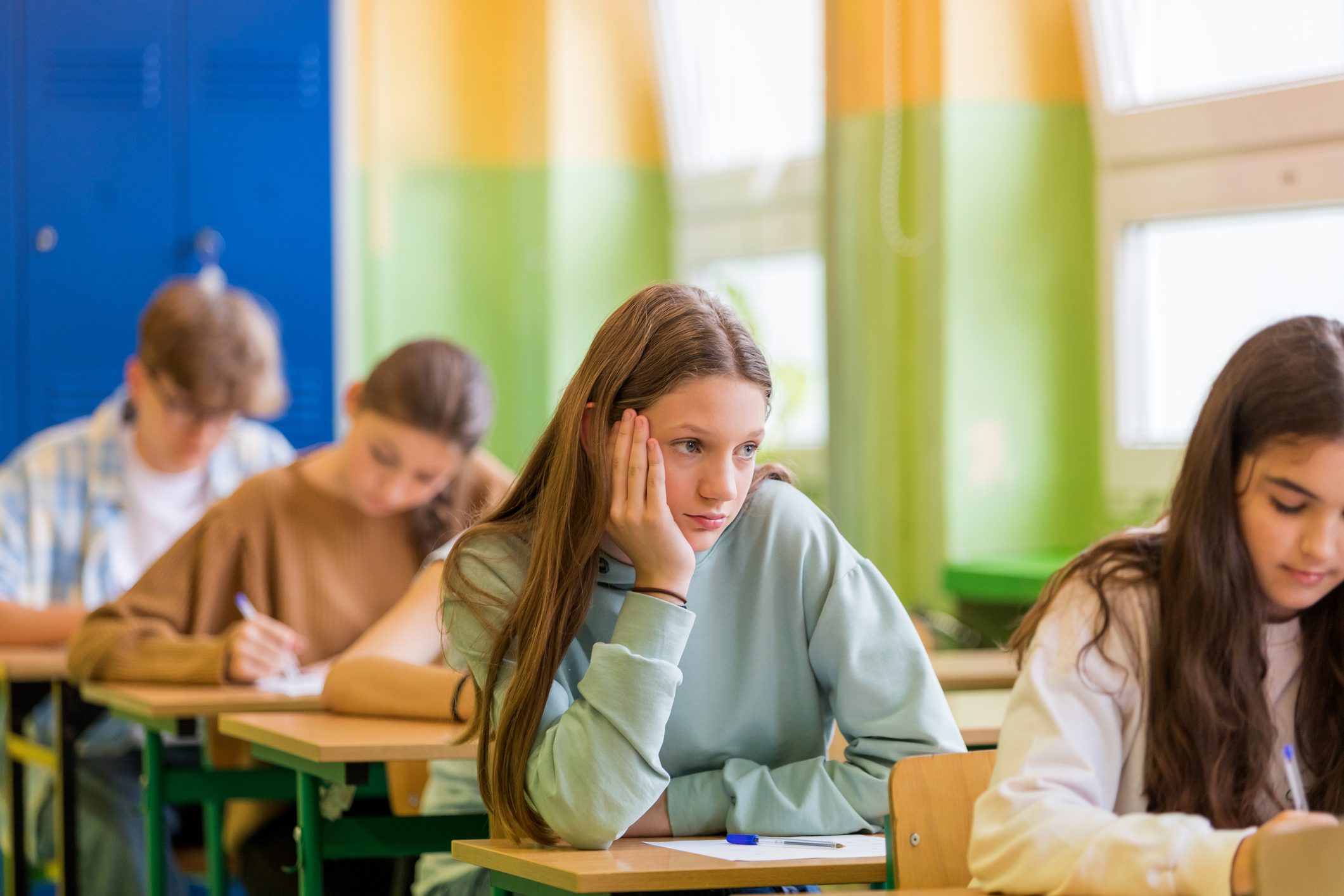 Bored teenage girl sits in a classroom while her peers do homework