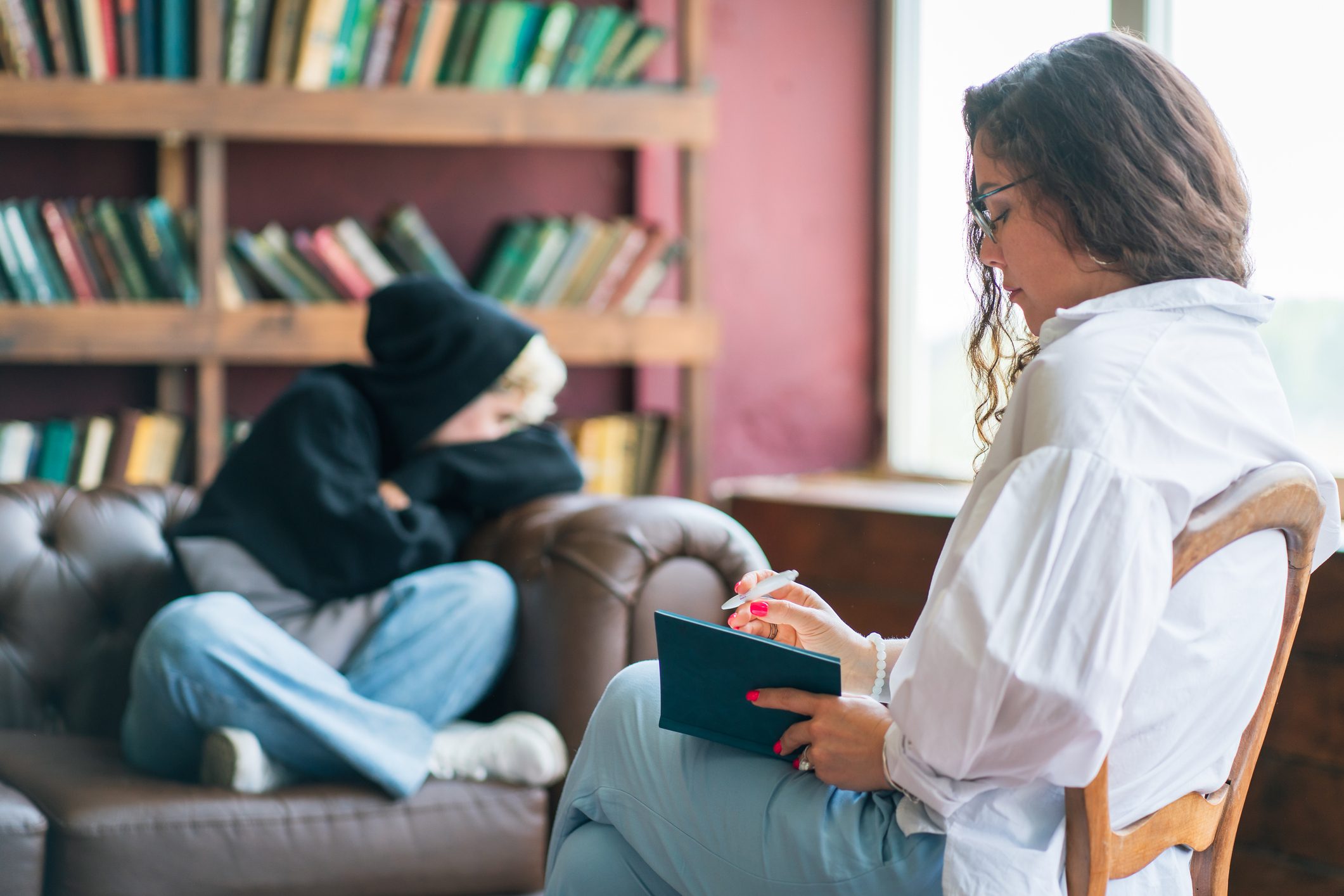 Teen in alcohol rehab therapy looks bored while therapist takes notes.